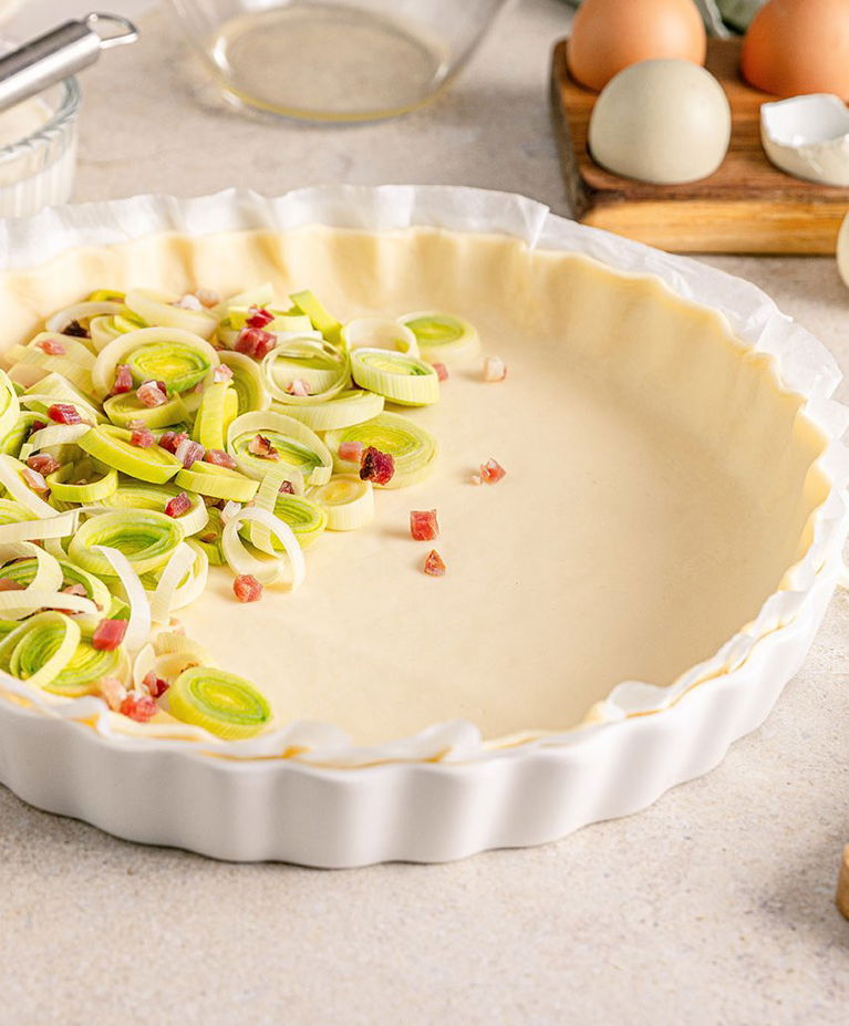 Nog ongebakken quiche en taartdeeg in de vorm met prei en hamblokjes erin