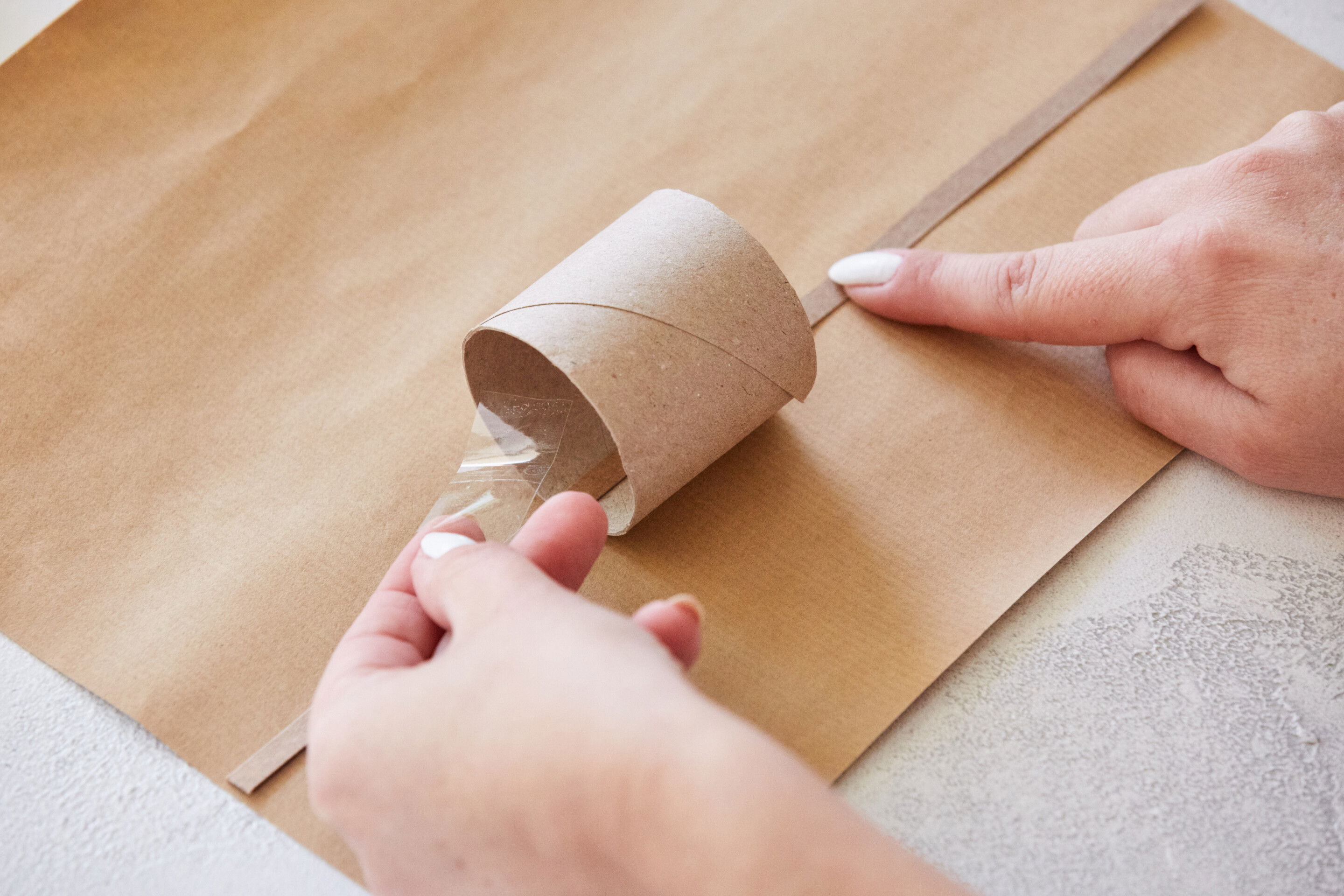 Schritt 3: Leg eine Hälfte der Klopapierrolle aufs Geschenkpapier. Fädle den Knallstreifen durch und fixiere Knallstreifen und Rolle mit einem Stück Klebeband am Geschenkpapier.